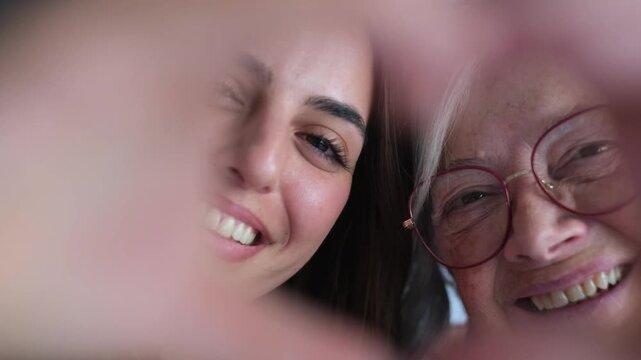 Generation gap bridged by love as a young woman and an older woman share a heartfelt moment, smiling through a hand-formed heart.