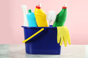 Bucket with toilet cleaning products and supplies on white marble table against pink background