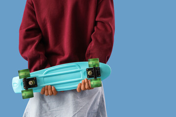 Young man with skateboard on blue background, back view © Pixel-Shot