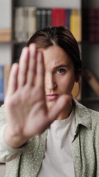 Woman palm STOP. Vertical video of frowning serious woman in office or room in apartment looking at camera raises her hand and shows her palm signaling STOP