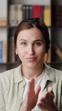 Woman sarcastic applause. Vertical video of gloomy skeptical woman in office or apartment looks at camera and reluctantly claps her palms to create fake applause