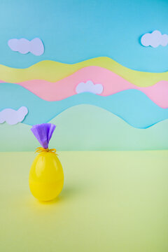Bright yellow easter egg wrapped as gift on pastel landscape background with clouds festive spring decoration concept.