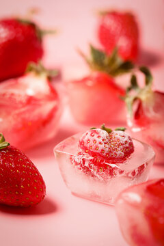 Frozen strawberries in ice cubes on pink background, closeup