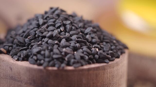 Macro shot of black cumin seeds in wooden bowl with oil background