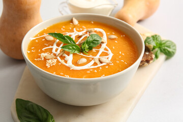 Bowl of delicious pumpkin cream soup with seeds and basil on white background