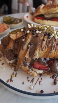 Delicious chocolate croissant with fresh strawberries and bananas, topped with pistachios and chocolate balls