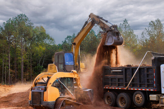 Heavy machinery digs transfers soil to dump truck at construction site at ground leveling