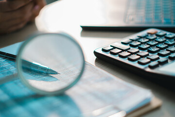 Close up of financial documents with calculator, pen and magnifying glass on desk, representing accounting, audit, business analysis, tax calculation and data verification in modern office environment