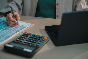 Close up of hand writing on financial report with pen, calculator and laptop on desk, representing accounting, business analysis, budgeting, tax preparation and financial data