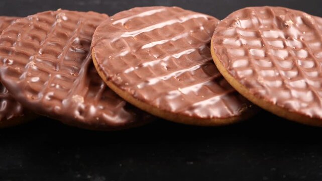 A close up slow motion view of delicious chocolate covered digestive biscuits arranged neatly on a dark background