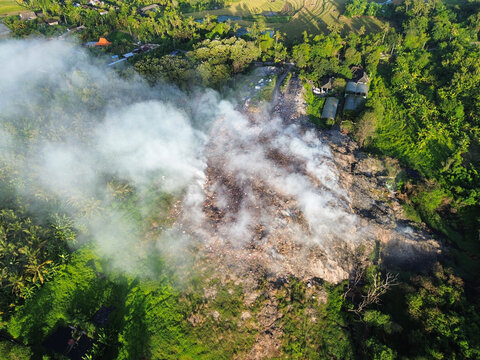 Aerial view of open trash burning at a rural landfill. Smoke rises into the air with scenic mountains in the background, highlighting the contrast between pollution and nature