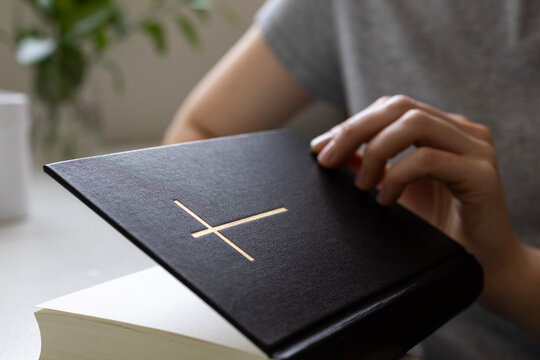 Close-up of a person opening a Bible with cross symbol. Christianity, faith, prayer and spiritual devotion concept