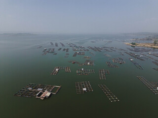 Aerial drone video of fish farming cages on a lake used for aquaculture and freshwater agriculture. Floating fish cages arranged in patterns on calm water. © Febriana