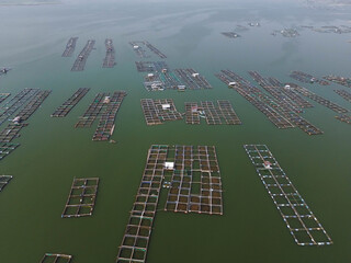 Aerial drone video of fish farming cages on a lake used for aquaculture and freshwater agriculture. Floating fish cages arranged in patterns on calm water. © Febriana
