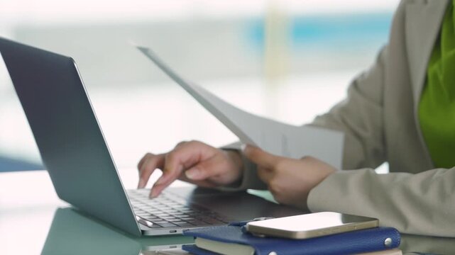 資料を見ながらノートパソコンに入力するビジネスウーマン 仕事中の日本人女性, Japanese Businesswoman Typing on Laptop While Checking Documents