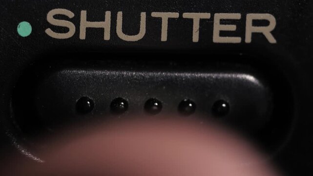 Macro close up of finger pressing shutter button with teal dot and grey lettering