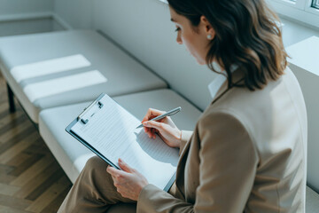 Naklejka premium High angle view of young adult woman writing notes on clipboard during consultation or interview, documenting assessment for healthcare, HR, or client intake marketing use