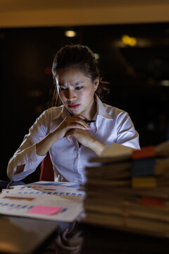 A young woman is intensely focused on analyzing documents at a desk, with stacks of papers around her, illuminated by a soft light, conveying a sense of concentration and urgency.