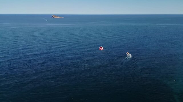 A parasailer being pulled by speed boat on tranquil blue ocean waters with distant island