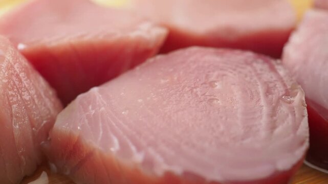Close up slow motion camera movement on fresh raw tuna fish fillets, showcasing the vibrant pink color and fine texture of the seafood, ready for cooking or preparing sushi on a wooden cutting board