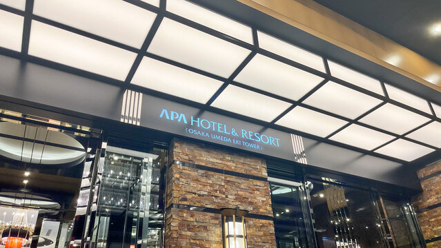 Illuminated night entrance of APA Hotel & Resort Osaka Umeda Eki Tower - Modern luxury hotel facade with stone walls and bright ceiling lights for travel and hospitality.