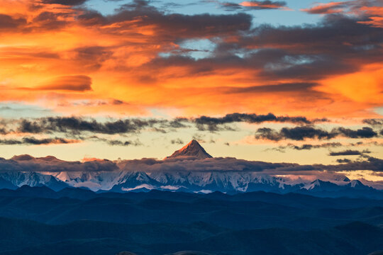 Mount Gongga (Minya Konka), the highest peak in Sichuan Province, China, rises above layered mountain ranges under a dramatic sunset sky.