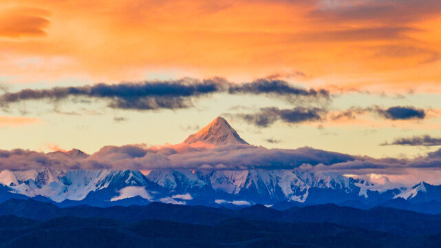 Mount Gongga (Minya Konka), the highest peak in Sichuan Province, China, rises above layered mountain ranges under a dramatic sunset sky.