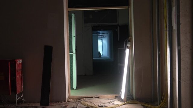 Empty construction hallway with temporary lighting and open doors, unfinished interior space with cables and raw walls, moody corridor in building under construction