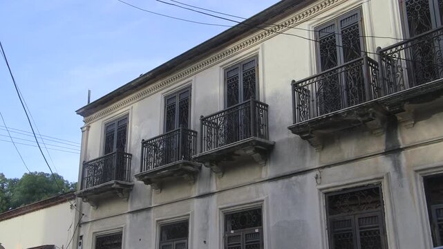 Neoclassical Spanish colonial structure featuring characteristic rejas (iron grilles) on multi-pane windows, projecting balconies, and subtle cornice detailing under clear blue skies.