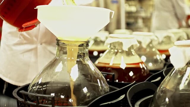 Liquid is poured through a funnel into a glass bottle during a controlled production process. Close up scene with transparent containers, measured filling and laboratory or industrial workflow.