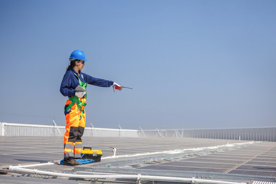 Engineer in safety harness inspecting solar panel installation on rooftop, Technician with walkie talkie during maintenance of photovoltaic system, Worker working on industrial solar power plant