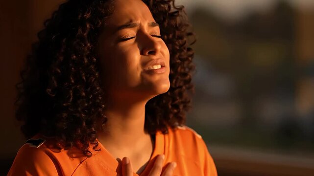 Close-up of a young mixed-race woman with eyes closed, singing her team's anthem with deep emotion and hand on heart.