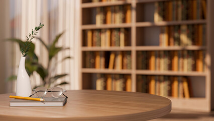 Eyeglasses and pencil on book with vase on round wooden table across bookshelf and window in library