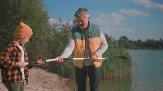 Dad teaches kayaking, Calm lakeside scene where father patiently teaches child proper paddle grip and safety precautions