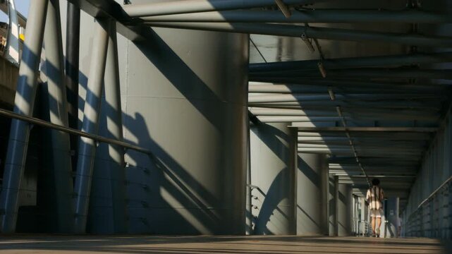 Dramatic perspective of an elevated walkway with steel tube roof structure casting striped shadows in golden morning light