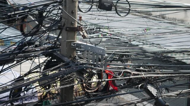 Chaotic tangle of electrical and fiber optic cables on a utility pole in a crowded urban street in Southeast Asia