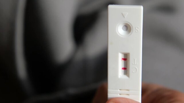 Positive rapid antigen test kit showing two red lines in closeup motion