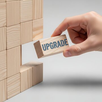 Hand placing a wooden block with the word upgrade into a wall made of blocks, representing progress and improvement