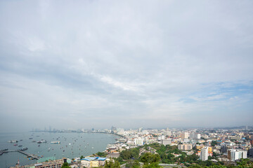 Naklejka premium Aerial view of a modern coastal city with buildings along the bay, boats on the sea, and a cloudy sky. Perfect for urban travel, architecture, and real estate business backgrounds.