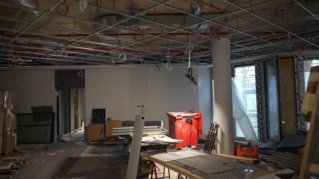 Unfinished construction interior with exposed ceiling grid and materials, open building space during renovation with cables, columns and work equipment