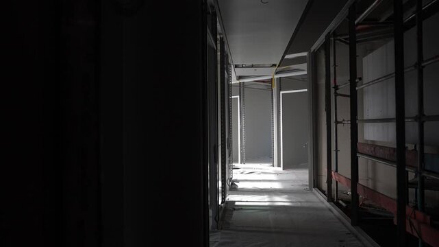 Unfinished corridor with drywall framing and light at end of hallway, interior construction space showing partition structure and buildout phase in modern building