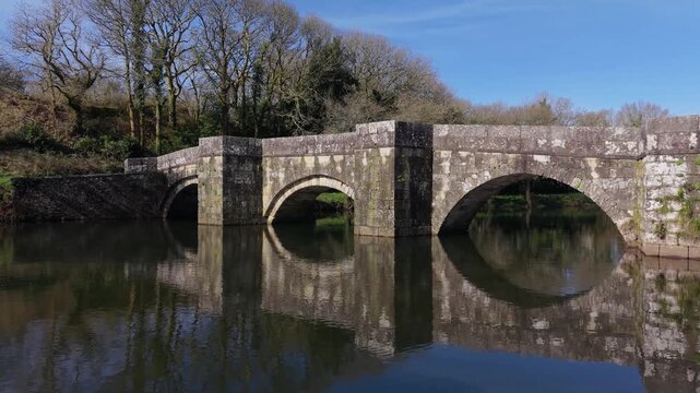 Reflections Of Ponte Romana de Brandomil (Brandomil Roman Bridge) Over Xallas River In Zas, Spain. Aerial Sideways Shot