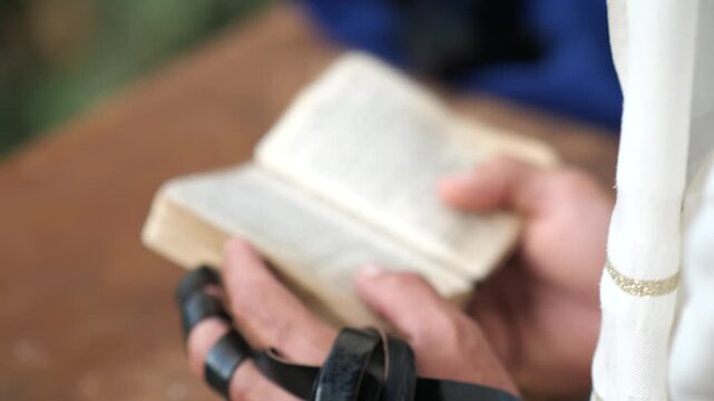 Close-up of tefillin on arm as man holds prayer book during prayer.