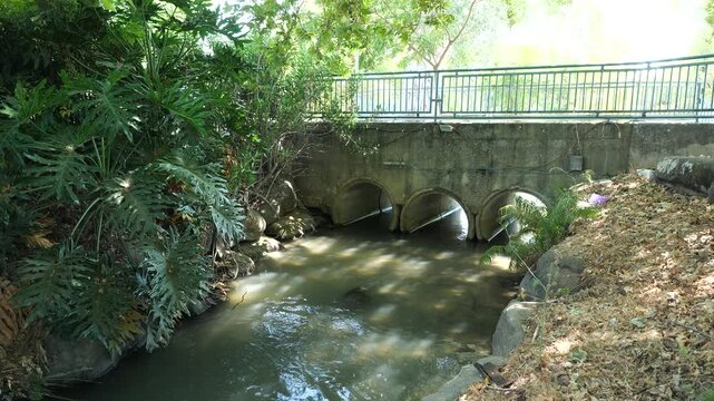 Stone bridge with arches over Nahal Hermon river in shaded area.