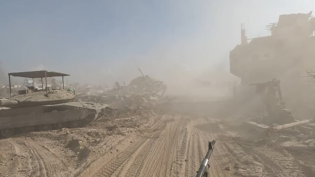Gaza Strip &mdash; POV from a military vehicle driving through a dusty street past an armored vehicle and heavily damaged buildings.