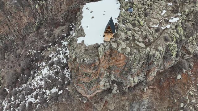 Aerial drone shot of luxury A-frame cabin on cliff in snowy mountains, remote winter travel destination 4K.