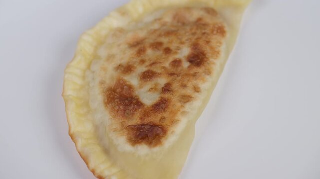Fried cheburek on plate detailed. Golden fried cheburek with crisp texture highlight. Studio shot capturing crispy cheburek on white plate with steaming hot surface details