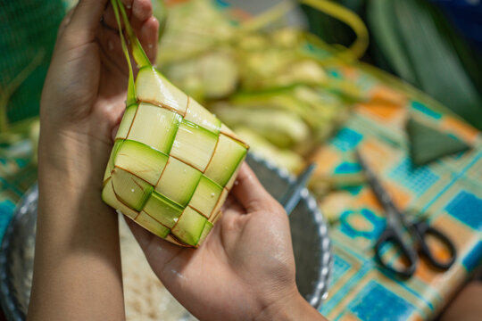 A close-up photo of hands holding a freshly woven ketupat, a traditional Indonesian rice dumpling, prepared for Eid al-Fitr celebrations in a warm, authentic atmosphere