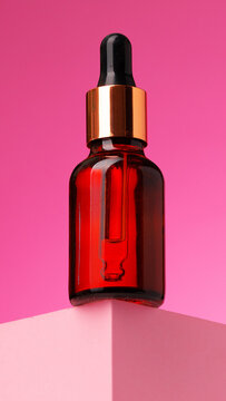Bottle of serum on a pink background with a simple display setup