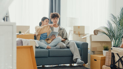 Young happy Asia couple sit on sofa couch use digital tablet online shopping furniture from decoration store in living room at home. Husband wife move new house, Apartment Rent And Ownership Concept. © tirachard